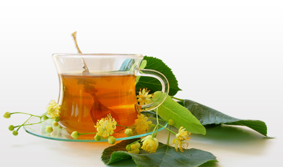 A glass cup of herbal tea with fresh blossoms and leaves