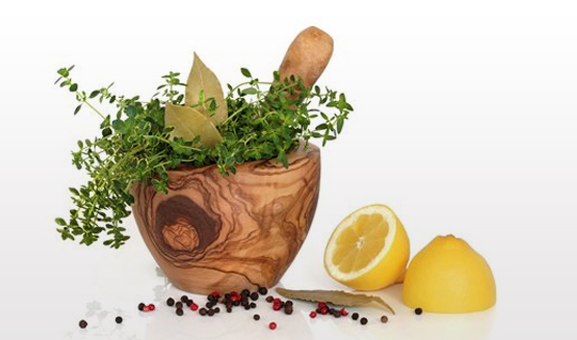 A wooden mortar filled with fresh thyme, beside lemon and peppercorns
