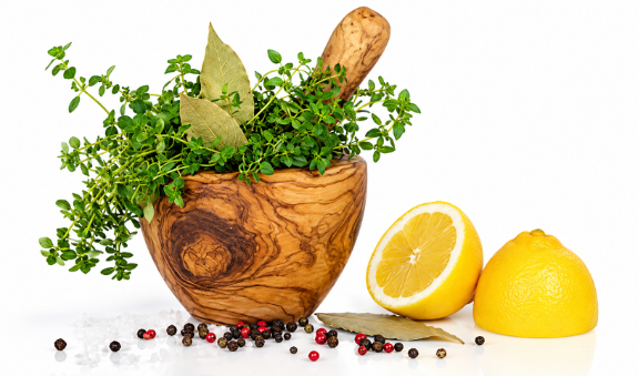Olive-wood mortar and pestle filled with fresh thyme and bay leaves, beside lemon, peppercorns and salt